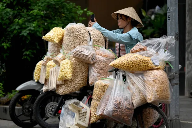  A street food vendor uses a mobile phone while waiting for customers on a street in Hanoi on April 17, 2026. (AFP) 