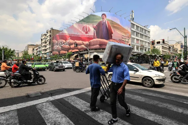 رجل يحمل طرداً على كتفه يمر أمام لوحة إعلانية كبيرة تصور المرشد مجتبى خامنئي في أحد شوارع طهران الاثنين (أ.ف.ب)