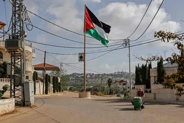 A worker walks past a Palestinian flag installed along a street in Turmus Ayya village, north of Ramallah in the Israeli-occupied West Bank on April 19, 2026. (AFP)