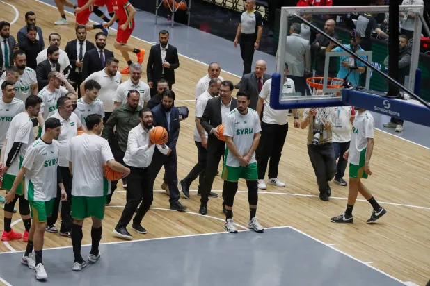 الرئيس السوري أحمد الشرع (وسط الصورة إلى اليسار) يسدد رمية حرة قبل مباراة ودية بين المنتخبين السوري واللبناني في حفل إعادة افتتاح صالة الفيحاء لكرة السلة بدمشق (أ.ب)