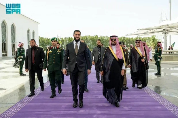 This handout picture provided by the Saudi Press Agency (SPA) shows the Deputy Governor of the Makkah Region Prince Saud bin Mishaal bin Abdulaziz, (C-R) welcoming Syrian President Ahmed al-Sharaa upon his arrival in Jeddah, on April 21, 2026. (SPA) 