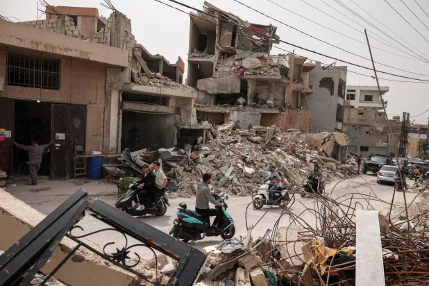 أشخاص يسيرون بجوار أنقاض المنازل التي دمرتها الغارات الإسرائيلية في طير دبا بجنوب لبنان (رويترز)