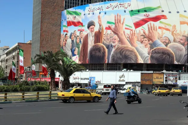 رجل إيراني يسير بجوار ملصق للمرشد الإيراني الراحل علي خامنئي في ساحة في طهران - 22 أبريل 2026 (إ.ب.أ)