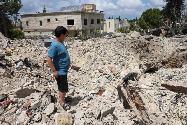 A child stands on the rubble of a building destroyed by an Israeli air strike in the southern Lebanese town of Kfarsir (AFP)
