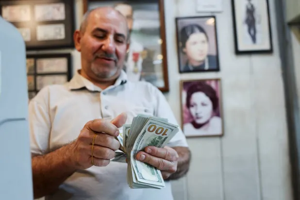 عامل يعدّ أوراقاً نقدية من فئة الدولار داخل محل صرافة ببغداد (أ.ف.ب)