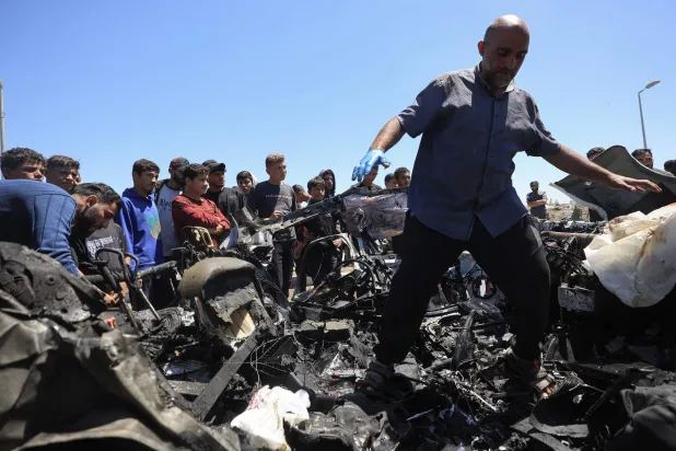 فلسطينيون في موقع استهداف سيارة بغارة جوية إسرائيلية في شارع صلاح الدين جنوب مخيم البريج وسط غزة الخميس (أ.ف.ب)