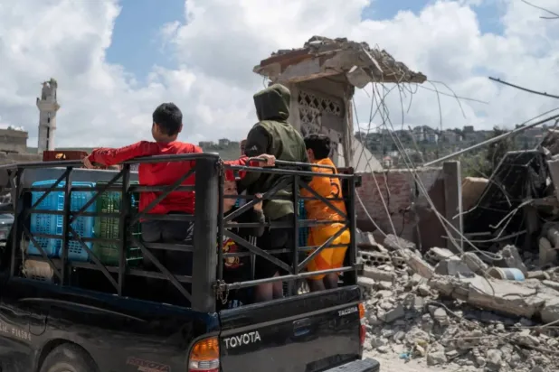 Children stand on a pickup truck as they pass damaged buildings after an Israeli airstrike in the southern Lebanese town of Mansouri (Reuters)
