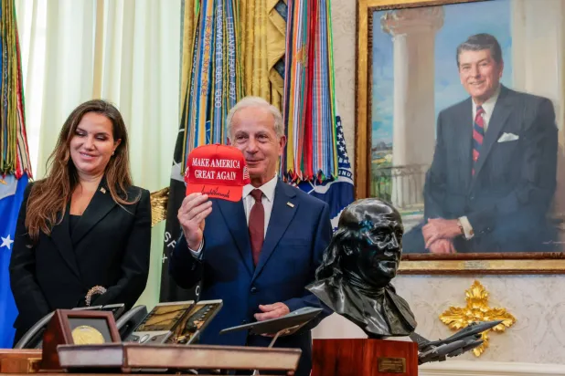 السفير الأميركي في لبنان ميشال عيسى يرفع قبعة كتب عليها «فلنجعل أميركا عظيمة مجدداً» موقعة من الرئيس دونالد ترمب بجوار السفيرة اللبنانية في الولايات المتحدة ندى حمادة معوض في المكتب البيضاوي بالبيت الأبيض - واشنطن العاصمة (رويترز)