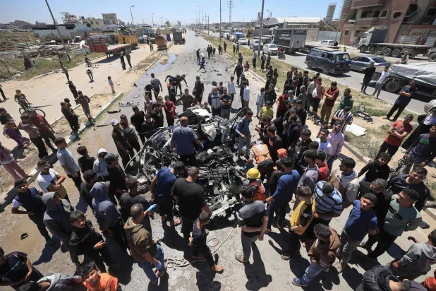 فلسطينيون يتجمَّعون حول سيارة مُدمَّرة بعد استهدافها بغارة إسرائيلية في شارع صلاح الدين جنوب مخيم البريج بقطاع غزة (أ.ف.ب)