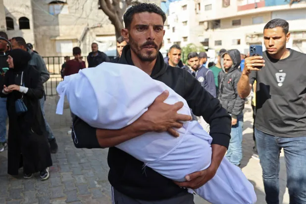 رجل يحمل جثمان طفل أمس السب تقتل جرَّاء قصف مدفعي إسرائيلي على منازل سكنية قرب مستشفى كمال عدوان في بيت لاهيا شمال قطاع غزة (أ.ف.ب)