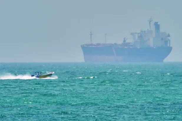 İran'ın Keşm adası açıklarında, Hürmüz Boğazı'nda bir sürat teknesi kargo gemisinin yakınından geçiyor (AP)