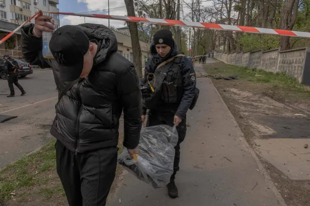 شرطي أوكراني (يمين) ويساعده رجل آخر يحملان كيساً بلاستيكياً يحتوي على حطام طائرة مسيّرة بموقع غارة روسية بطائرة مسيّرة في كييف 28 أبريل 2026 (أ.ف.ب)