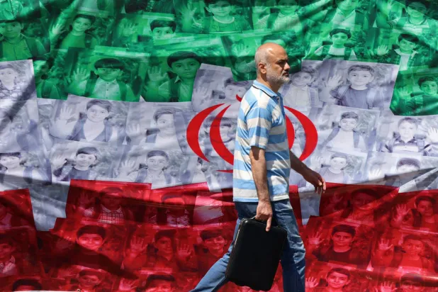 A man walks past an Iranian flag installed along the roadside in Tehran on April 29, 2026, depicting images of children killed on the first day of the war in an alleged US-Israeli missile strike on a school in the southern Iranian city of Minab. (Photo by ATTA KENARE / AFP) 