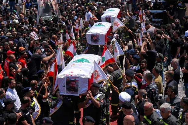 يحمل المشيعون نعوش ثلاثة من عناصر الدفاع المدني اللبناني الذين استشهدوا في غارة جوية إسرائيلية على بلدة مجدل زون خلال جنازتهم في مدينة صور الجنوبية (رويترز)