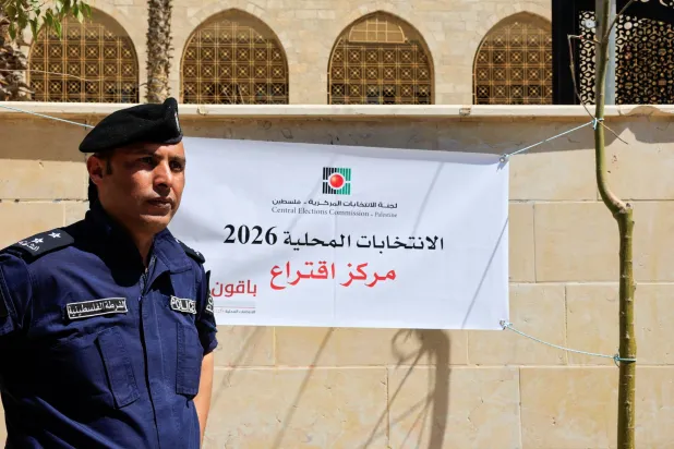 A police officer stands next to a banner at a polling station during the municipal council election, in Hebron, in the Israeli-occupied West Bank, April 25, 2026. REUTERS/Mussa Qawasma
