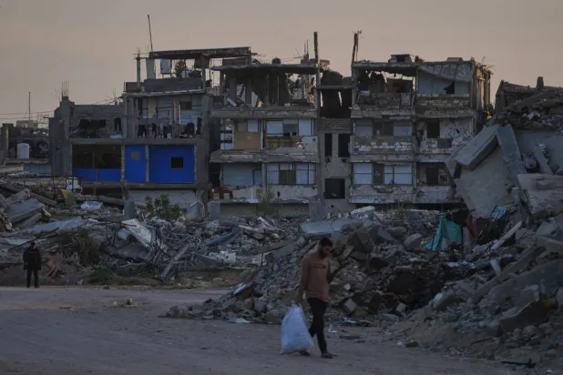 FILE - Palestinians walk along a street surrounded by buildings destroyed during Israeli air and ground operations in Khan Younis, southern Gaza Strip, on April 9, 2026. (AP Photo/Abdel Kareem Hana, File)