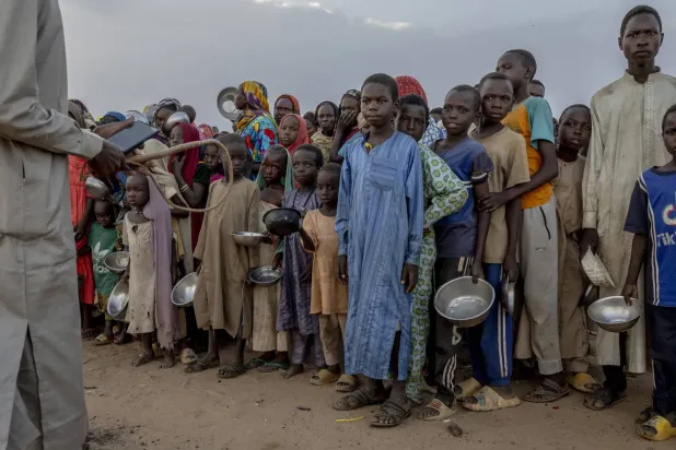 Sudan-Çad sınırında yer alan Adré (Adri) Mülteci Kampı’nda bir grup Sudanlı mülteci çocuk yemek almak için itişip kakışırken, elinde kırbaç tutan bir adam onları kontrol altına almaya çalışıyor (NYT)
