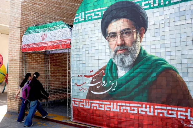 Women walk past a banner depicting Iran's current supreme leader Mojtaba Khamenei along a street Tehran on May 6, 2026. (Photo by AFP) 
