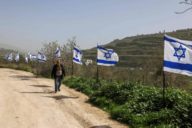 فلسطيني يمرّ بجوار سياج من الأعلام الإسرائيلية نصبه مستوطنون بعد استيلائهم على محطة قطار تعود إلى العصر العثماني في قرية برقة شمال الضفة فبراير الماضي (أ.ف.ب)