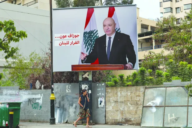 A woman walks past a billboard depicting Lebanese President Joseph Aoun and sentence reading in Arabic 'The decision is up to Lebanon' EPA/WAEL HAMZEH