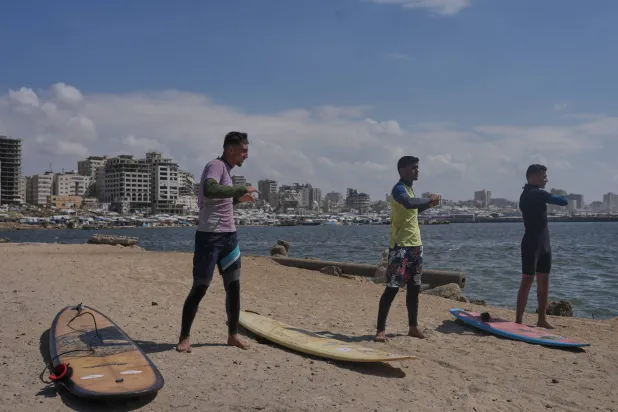Palestinians Tahseen Abu Assi, left, Khalil Abu Jayyab, center, and Abed Rahim Alostaz warn up before surfing on the beach in Gaza City, Monday, May 4, 2026. (AP Photo/Jehad Alshrafi)