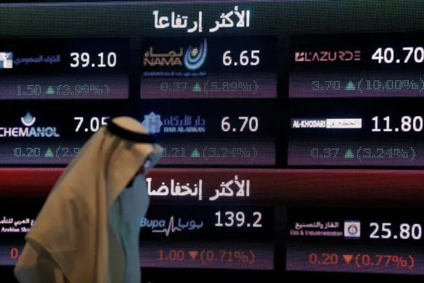 مستثمر يمر أمام شاشة تعرض معلومات سوق الأسهم السعودية في الرياض (رويترز)