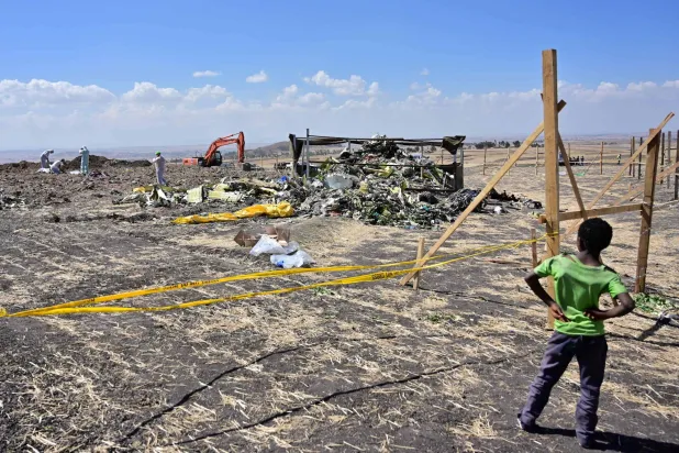 (FILES) A boy looks as forensic investigators comb the ground for DNA evidence near a pile of twisted airplane debris at the crash site of an Ethiopian airways operated Boeing 737 MAX aircraft on March 16, 2019 at Hama Quntushele village near Bishoftu in Oromia region. (Photo by TONY KARUMBA / AFP)