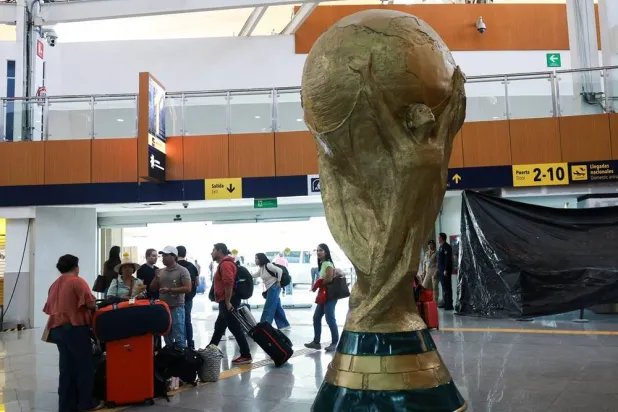  Passengers stand beside a giant replica of the World Cup trophy displayed at Mexico City International Airport, ahead of the World Cup starting on June 11, in Mexico City, Mexico, May 15, 2026. (Reuters)