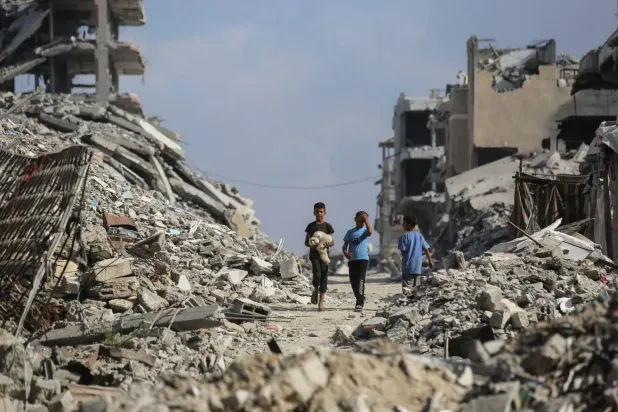 Gazze Şeridi’nin batısında bulunan eş-Şati Mülteci Kampı’ndaki binaların enkazı arasında yürüyen Filistinli çocuklar (AFP)