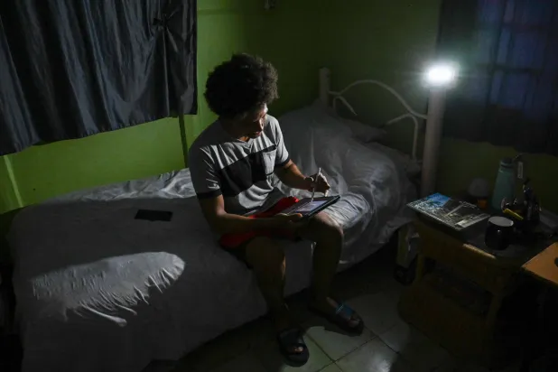 Alfredo Rodriguez, industrial designer and ISDI professor, studies during a power cut in Punta Brava, Havana on May 11, 2026. (AFP)