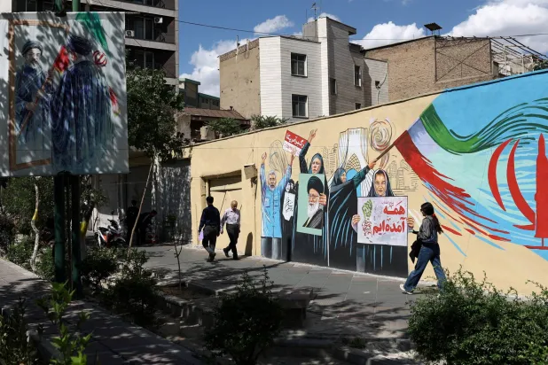 أشخاص يسيرون بجانب جدارية جدارية تحمل صورة المرشد الايراني السابق علي خامنئي في أحد شوارع طهران (رويترز)