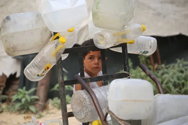 A Palestinian boy stands next to plastic containers on a trolley, as he and others collect portable drinking water for their displaced family living in shelters after homes were destroyed in Israeli bombardment, in the Bureij refugee camp, in the central Gaza Strip on May 18, 2026. (AFP)