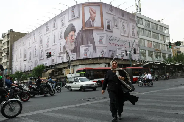 سيدة تسير في أحد شوارع طهران وفي الخلفية لافتة عملاقة تحمل صورة المرشد السابق علي خامنئي (رويترز)