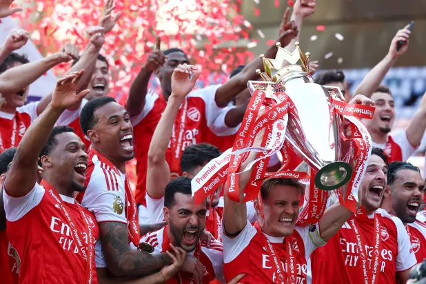 مارتن أوديغارد يرفع الكأس وهو يحتفل مع زملائه بعد الفوز بالدوري الإنجليزي الممتاز (رويترز)