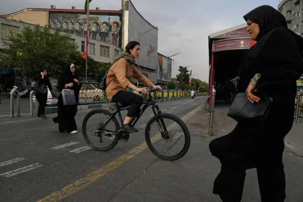 A woman rides a bicycle as others cross a street in downtown Tehran, Iran, Sunday, May 24, 2026. (AP)