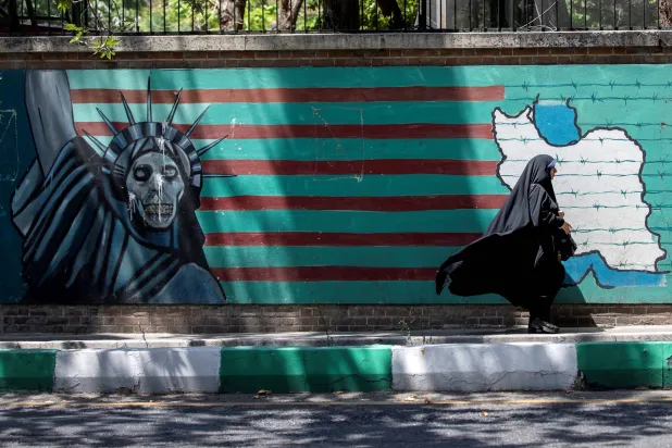 إيرانية تمر أمام جدارية معادية لواشنطن في طهران، وتُظهر العلم الأميركي محاطاً بالأسلاك الشائكة وتمثال الحرية بوجه على هيئة جمجمة (أرشيفية_رويترز)