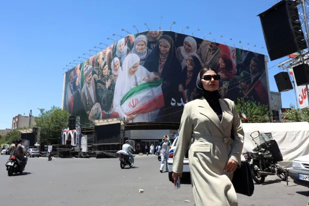 A woman walks next to a huge billboard in a street in Tehran, Iran, 25 May 2026. EPA/ABEDIN TAHERKENAREH