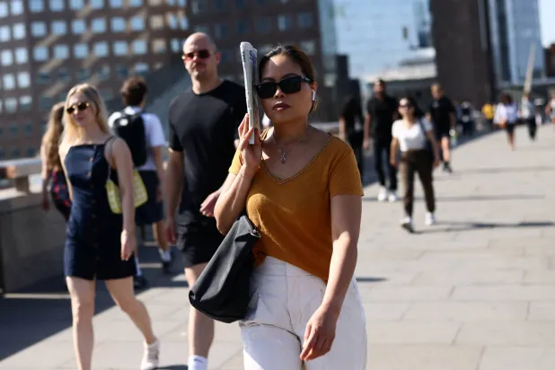 A woman shields herself from the sun with a newspaper as she crosses London Bridge during a heatwave in London, Britain, May 26, 2026. REUTERS/Jack Taylor