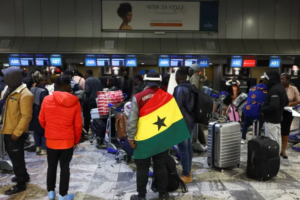 A man draped in a Ghana flag stands among other Ghanaians as Ghana repatriates hundreds of its citizens from South Africa following instances of violence against migrants from other sub-Saharan African countries, amid a wave ‌of protests against illegal immigration, at O.R. Tambo International Airport in Kempton Park, South Africa. REUTERS/Siphiwe Sibeko 