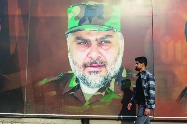 An Iraqi man walks past a poster of Moqtada al-Sadr wearing Saraya al-Salam military uniform on a street in Baghdad (AFP)