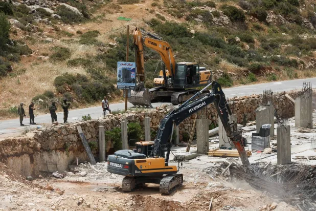 آليات إسرائيلية ثقيلة تهدم مبنى في قرية الولجة الفلسطينية بالضفة الغربية المحتلة يوم 18 مايو الحالي (رويترز)