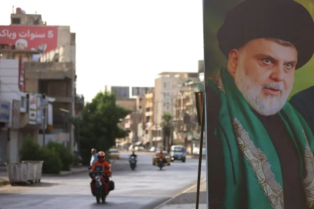 دراجة نارية تمر أمام لافتة لمقتدى الصدر نُصبت على أحد شوارع بغداد 27 مايو 2026 (أ.ف.ب)