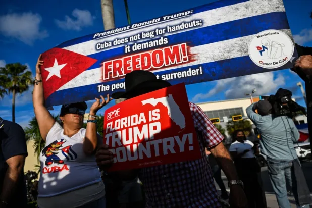 Miami'deki Versailles restoranının önünde, ABD'nin eski Küba Devlet Başkanı Raúl Castro'ya yönelttiği suçlamaları destekleyen pankartlar taşıyan insanlar, 20 Mayıs 2026 (AFP)
