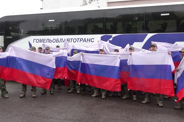 This video grab taken from a handout footage released by the Russian Defense Ministry on May 15, 2026, shows Russian prisoners of war (POWs) posing with flags in front of a bus following an exchange of prisoners at an undisclosed location in Belarus. (AFP / Russian Defense Ministry/ Handout) 