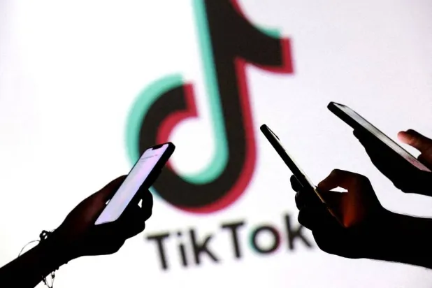 Teenagers pose for a photo while holding smartphones in front of a TikTok logo in this illustration created on September 11, 2025. (Reuters)
