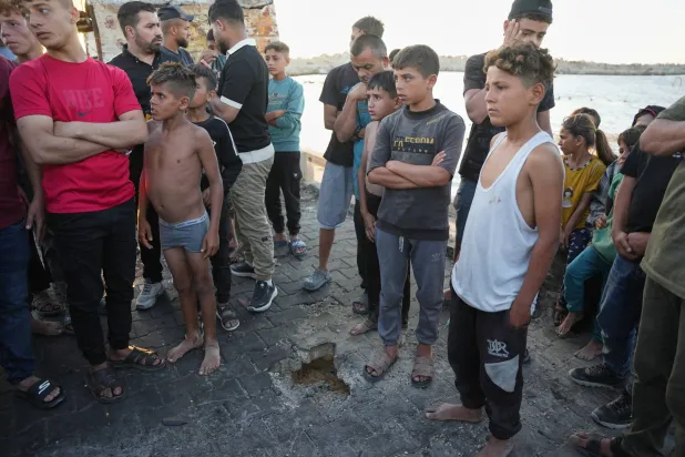 فلسطينيون يقفون قرب موقع سقوط شظايا غارة إسرائيلية في ميناء مدينة غزة يوم الأحد (أ.ب)