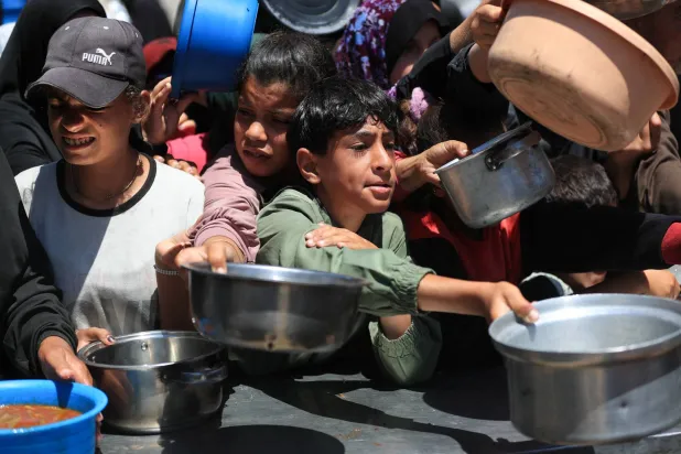فلسطينيون ينتظرون لتلقي الطعام من مطبخ خيري في مدينة غزة يوم الثلاثاء (رويترز)