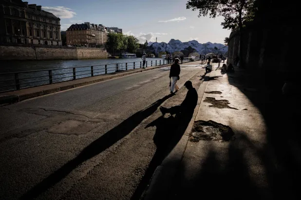 People walk along the Seine river in Paris on June 2, 2026 with in the background "La Caverne du Pont Neuf" ("The Pont Neuf Cave") artwork by French street artist and photographer JR on the Pont-Neuf bridge after it was damaged and torn by the wind. (Photo by SIMON WOHLFAHRT / AFP) 
