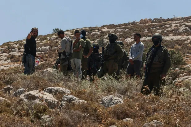 قوات إسرائيلية ومستوطنون مسلحون يقفون قبالة احتجاج لفلسطينيين على مصادرة أراضيهم قرب الخليل في الضفة الغربية المحتلة الثلاثاء (أ.ف.ب)
