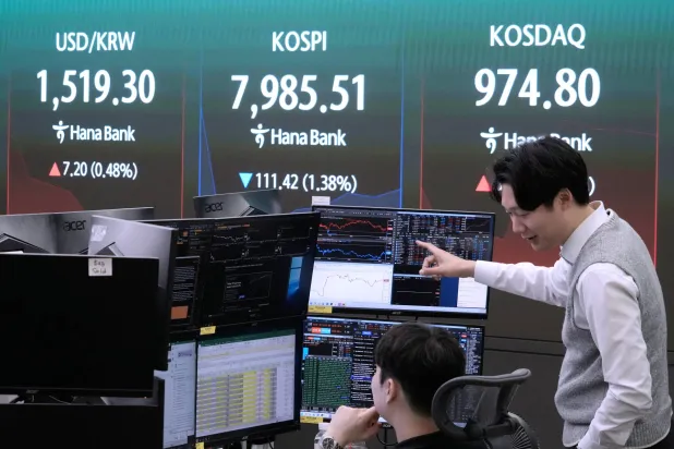 متداولان في بنك هانا وبجانبهما شاشة تعرض مؤشر «كوسبي» وسعر صرف الدولار والوون الكوري الجنوبي (أ.ب)